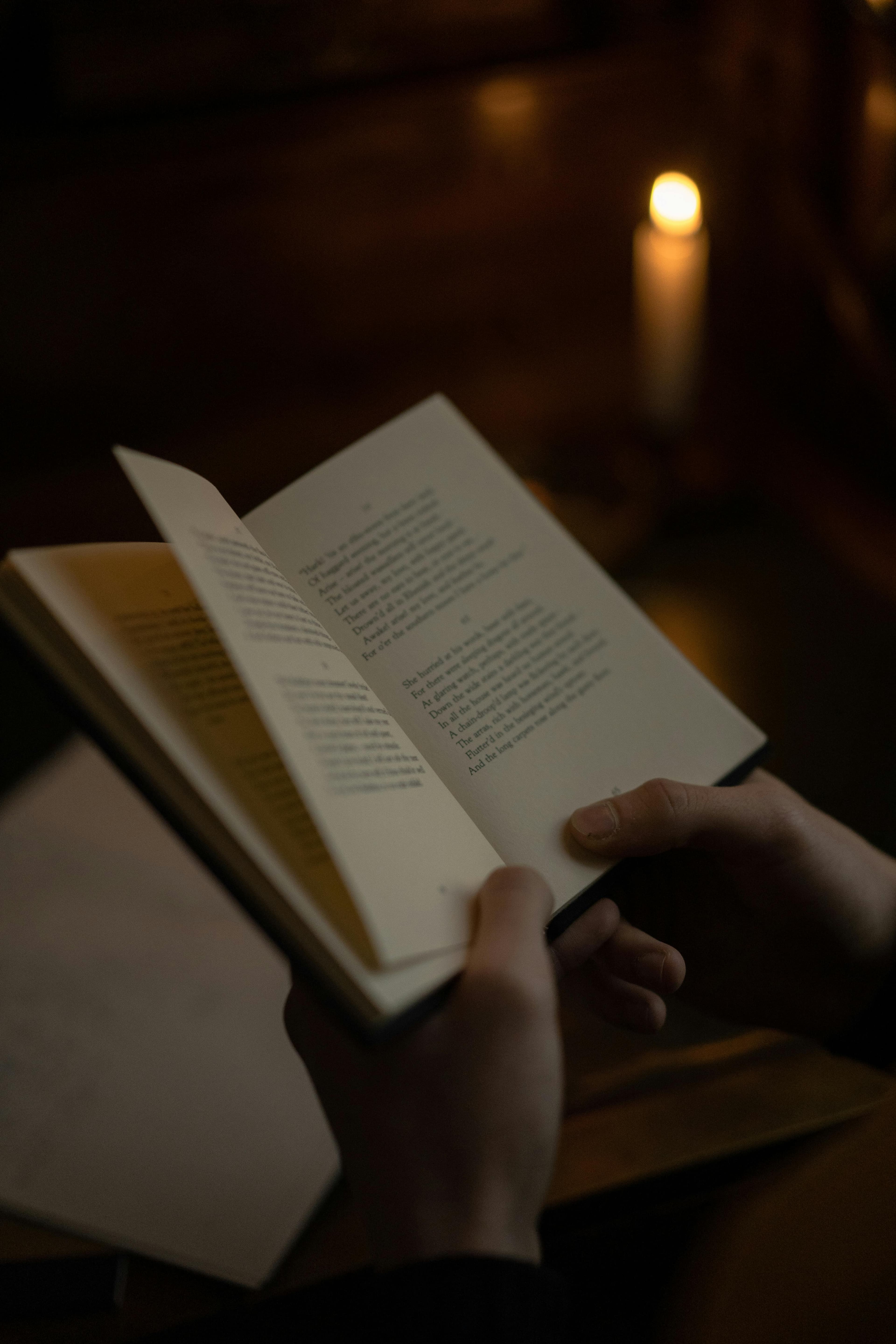 Hands reading an open book beside candlelight